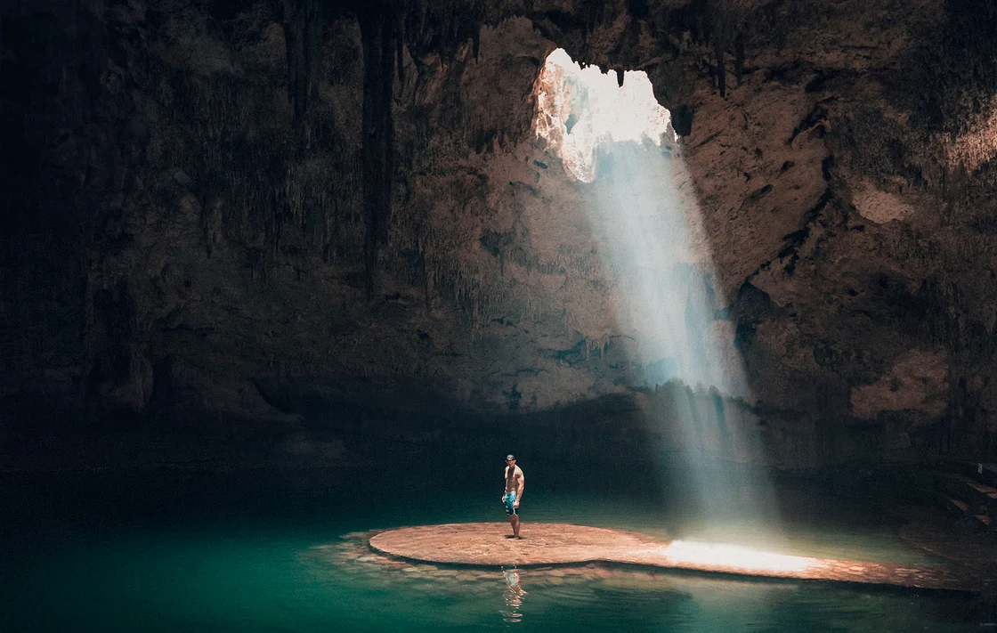 Uomo dentro una grotta con un laghetto e uno spiraglio di luce