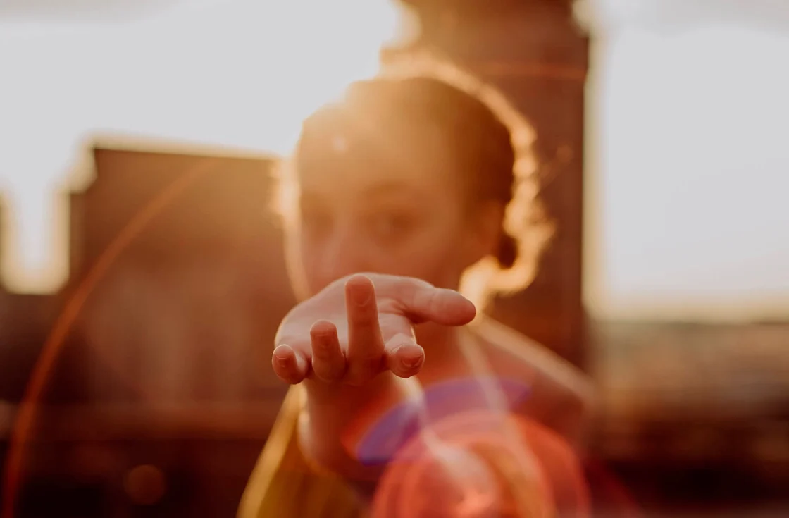 Bambina sotto la luce del sole che guarda dritto con la mano stesa